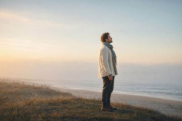 A person is standing in soft morning light, visibly relaxed, symbolizing the moment the body stops bracing.